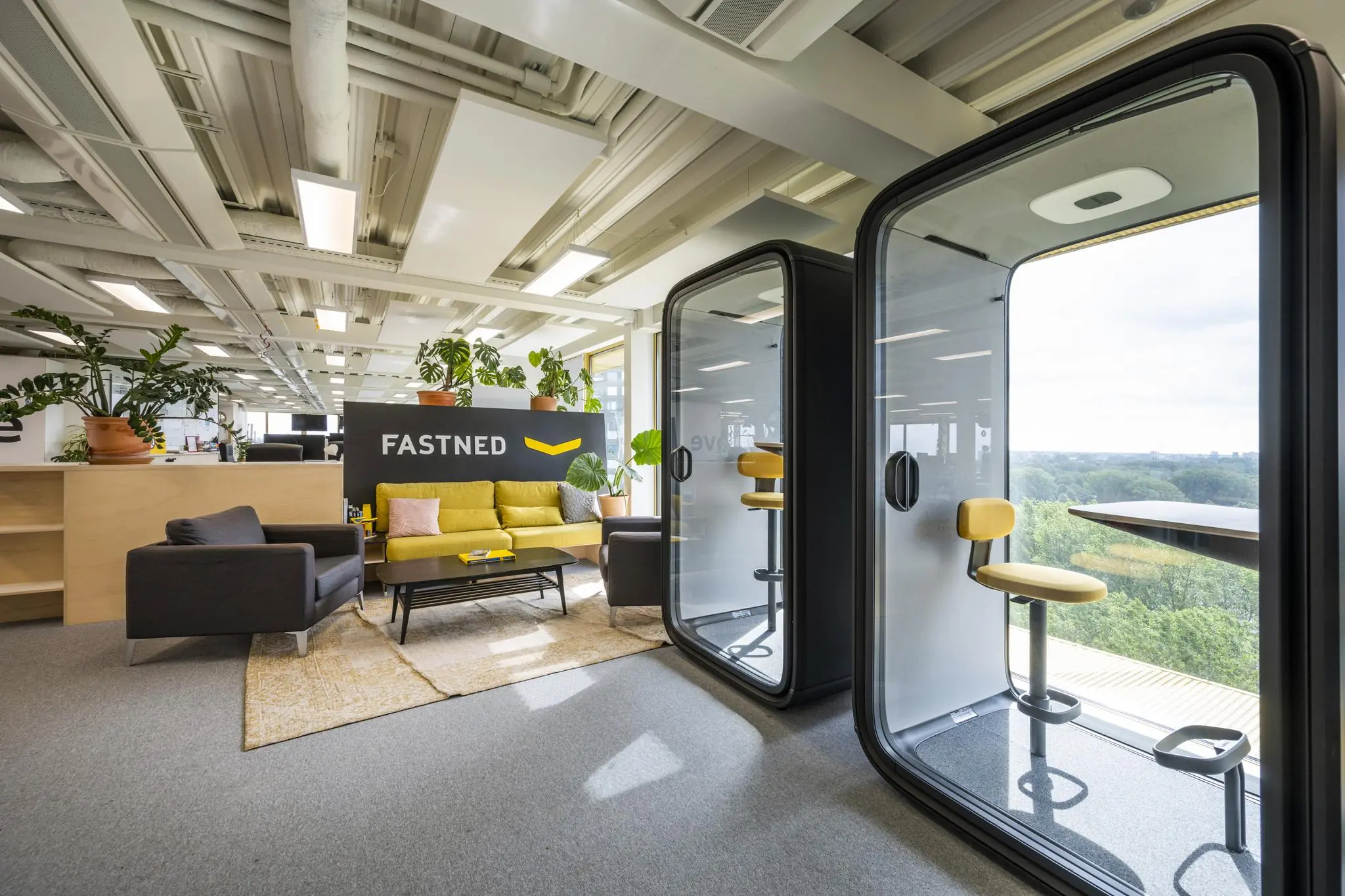 Modern kantoorinterieur van Fastned aan de James Wattstraat met loungehoek, belcabines en uitzicht op groen landschap.